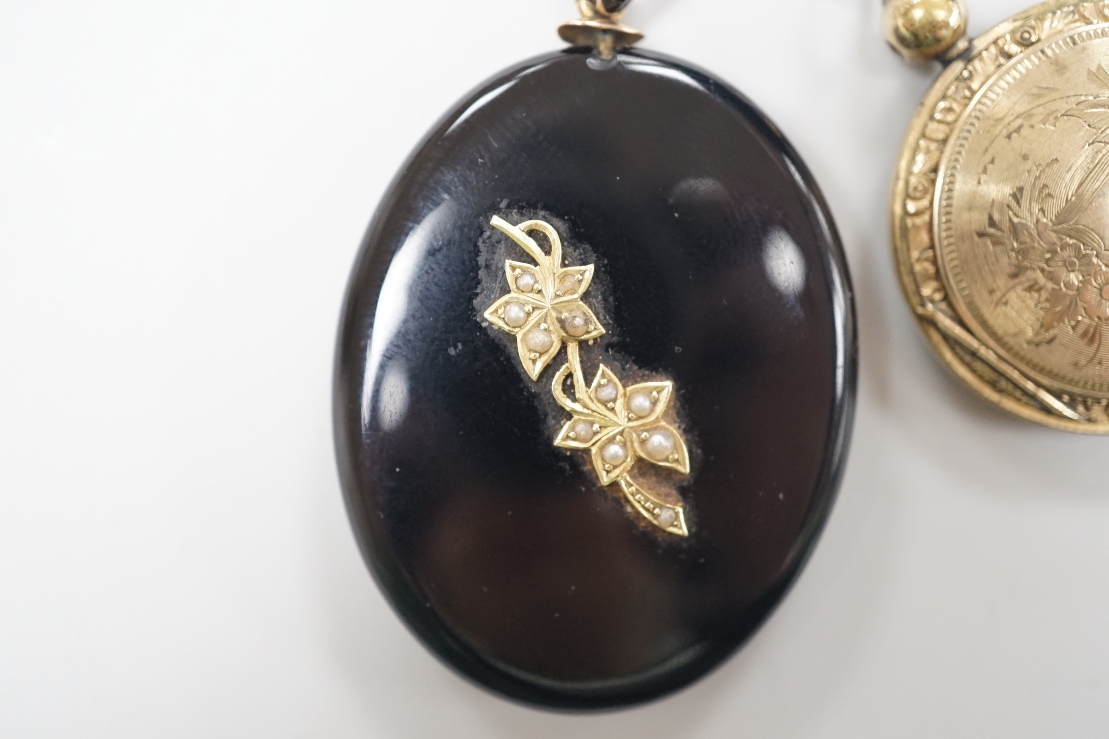 A Victorian yellow metal and seed pearl mounted black onyx oval pendant locket, with enamelled bale, overall 53mm and an engraved gold plated circular pendant locket.